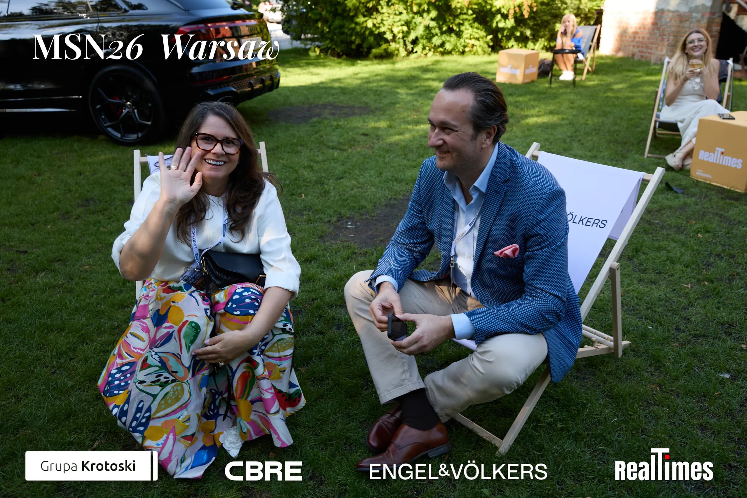 Mid-Summer Night 2026 at B'Fort, Warsaw: same pair laughing in garden deckchairs
