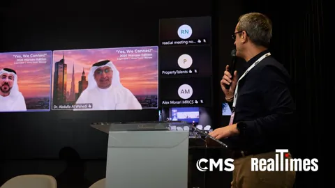 Alexander Morari at the lectern, turning to Dr Abdulla Al Wahedi on screen, at Yes, We Cannes! 2026 in Warsaw.