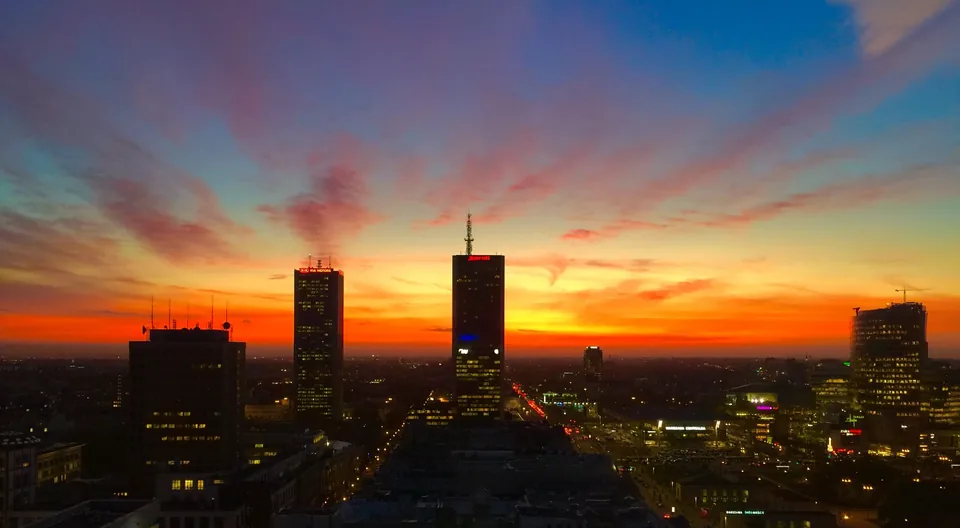 Warsaw city-centre towers in silhouette against a red and orange sky at dusk.