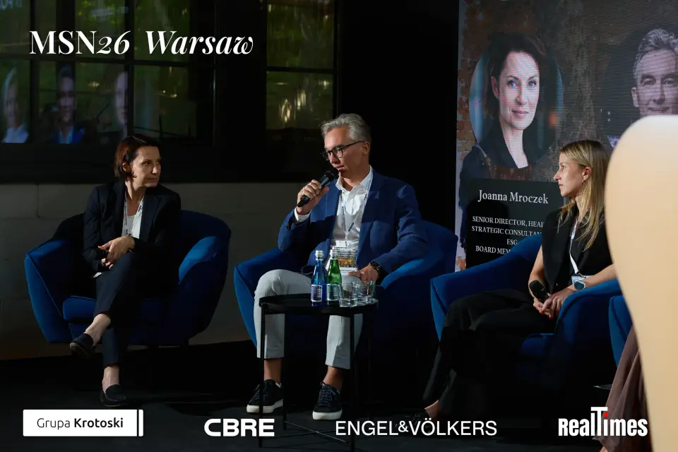 Mid-Summer Night 2026 at B'Fort, Warsaw: man with mic + panelists, Mroczek card behind