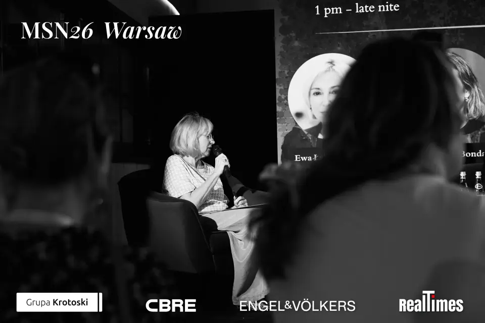 Mid-Summer Night 2026 at B'Fort, Warsaw: b&w moderator on stage, audience foreground